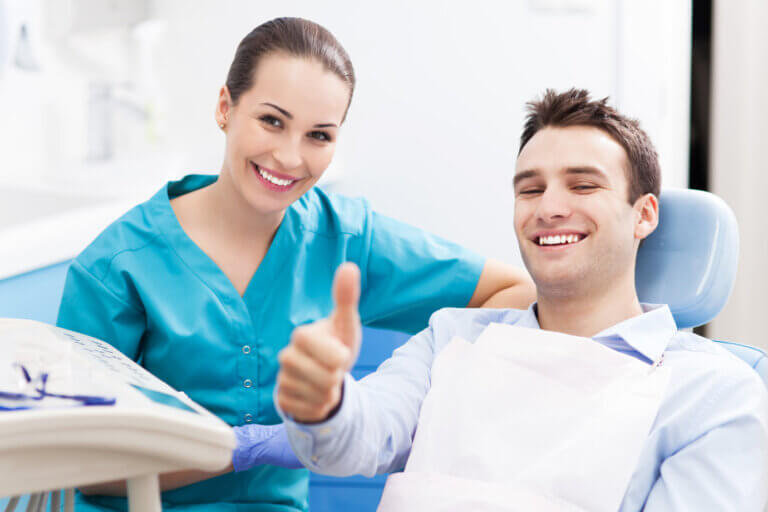 Man giving thumbs up at dentist office sitting beside female dentist