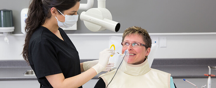 Female patient wearing a lead apron getting digital x-ray image taken by a female dental assistant